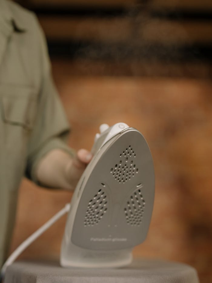 gallery-2 A close-up image captures a hand holding a steam iron indoors, showcasing home care.